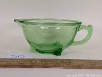 Side profile photo of the green glass batter bowl showing the spout, handle, and three legs, with measuring ruler for scale.