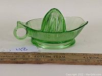 Side view of green depression glass citrus juice reamer alongside a ruler for scale showing approximately 6 inch length with handle