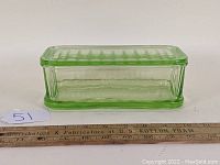 Front view of green Depression glass rectangular refrigerator dish with lid and measuring ruler for scale.