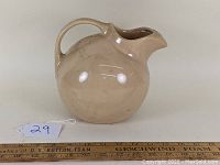 Side view of tan spherical ball pitcher showing handle and body with measuring ruler for scale.
