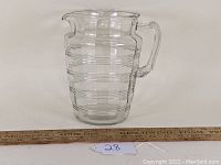 Clear glass Hocking Glass Co. pitcher with banded ring pattern, placed next to a ruler showing scale.