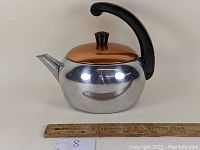 Front side view of the shiny aluminum tea kettle displaying the copper anodized lid, black Bakelite handle, and short spout.