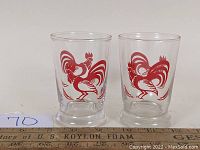 Pair of vintage clear glass tumblers with large red rooster prints shown from the front with a ruler for scale.