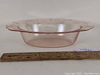 Side view of the pink Depression glass oval vegetable bowl showing the detailed scalloped rim and pattern with a ruler for size reference.