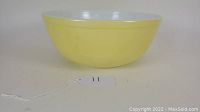 Yellow Pyrex mixing bowl with white interior shown from a side angle.