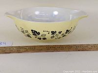 Side view of the yellow vintage Pyrex bowl with black gooseberries and leaves pattern, showing the shape and size relative to a ruler.