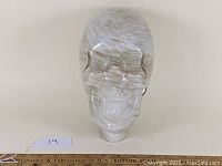 Front view of the glass skull showing white and gold streaked pattern.