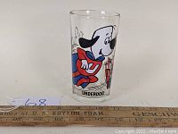 Front view of vintage Underdog Pepsi glass with Underdog character and cityscape background, ruler included for scale.