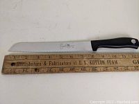 Two Wusthof Emeril serrated bread slicer knives laid beside 18-inch wooden ruler for scale, showing knives are about 12 inches total length with 8-inch blades.
