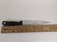 Full length of utility knife with black handle laid against ruler showing blade length about 20 cm.