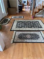 Four area rugs displayed on hardwood floor including large rug, narrow runner and two smaller rugs with black and cream designs