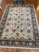 Full view of the large cream and black oriental area rug laid on wood floor