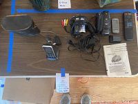 Top view of binoculars case, camcorders with cords and remotes on table.