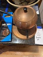 Copper fondue pot on stand with lid and six fondue forks in original packaging visible.