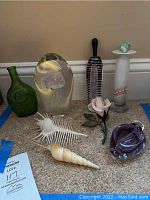 Overview of the assortment on carpet showing green glass jar, clear glass flower paperweight, striped glass stopper, purple heart shaped glass paperweight, shell objects, and flower figurine.
