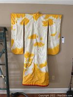 Full front view of yellow and white wedding kimono hung against wall