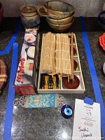 Photo of bamboo sushi mats, chopstick holders, art pottery cups and honey pot, boxed sushi knife, decorative tile and blue glass charm on kitchen countertop