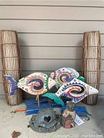 Photo showing four colorful hand-painted wooden fish sculptures on blue bases, two tall bamboo outdoor lights, ceramic cat figurine and metal turtle sculpture on porch.