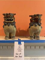 Pair of Foo Dog sculptures displayed side by side on a mantle, beige with blue and brown glazing, standing approximately 9 inches tall.
