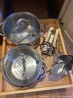 Stainless steel Rohe pots with lids, perforated steamer insert, and Sunbeam electric hand mixer with beaters and metal utensils in a drawer.