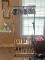 Full view of the wooden garment rack with hangers and two lower slatted shelves, positioned in front of a window.