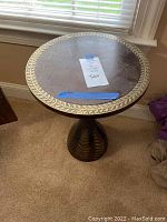 Angled front view of the side table showing the carved leaf border on top and general size relative to window and carpet.