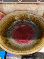 Top view of a ceramic bowl showing gradient glaze from red center to brown and green edges.