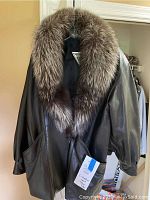 Front view of the black leather women's jacket with large natural-toned fox fur collar hanging on a hanger.