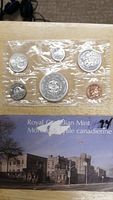 View of sealed plastic package with 7 Canadian coins from 1964, displayed with Royal Canadian Mint card showing the mint building.