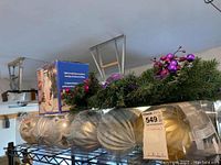 Wide view of Christmas decorations on metal shelving including large silver ornaments, artificial wreath with berries, blue boxed snowman figure
