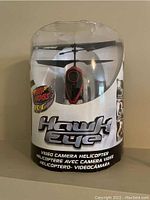 Front view of Hawk Eye RC helicopter in packaging showing red helicopter body with camera and dual black rotor blades clearly.