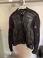 Front view of the men's black leather jacket with zipper and snap-button collar, padded shoulders and detailing on arms.