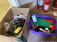 View of two containers with loose Lego pieces including technical and classic bricks, baseplates, wheels, and figures.