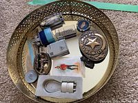 Photo of brass decorative mirror tray holding vintage lighters, belt buckle, pins, poker chip, token, and saw edge decorative item.