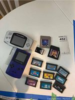 Top view of both Nintendo Game Boy consoles alongside eleven game cartridges and instruction booklet on a white surface.