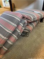Six stacked outdoor seat cushions with ties, striped fabric in muted reds, greens, grey and white, visible stains on fabric.