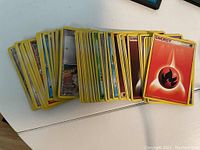 Pile of assorted Pokemon cards with yellow borders including energy and character cards spread on a white surface