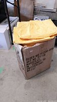 Yellow rain ponchos folded and placed on top of a cardboard box with product info printed on it.
