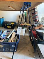 Side view of one metal sawhorse showing black legs, blue top, and wooden crossbar with metal braces.