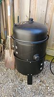Full view of black metal smoker grill showing lid, mid-section, and bottom firebox with door closed.
