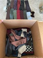 Box filled with various men's neckties and one brown velvet bow tie inside.