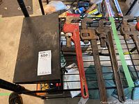 Photo showing four pipe wrenches placed on top of a black metal toolbox, the pipe wrenches have red and dark handles with significant wear and rust present.