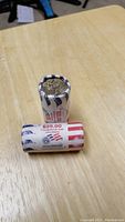 Two rolls of US $1 Presidential coins wrapped in paper, one standing upright and the other laying down showing the $25 face value and John Adams name on the wrapper.