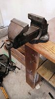 Metal bench vise mounted on wooden workbench, showing the full length and structure.