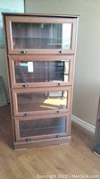 Front view of four-tier faux wood laminate barrister bookcase showing four framed glass doors with knobs.