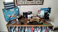 Full lot view on top of bookshelf showing boomerang on stand, model airplanes, coin boxes, dolphin sculptures, framed artworks, and other items.