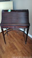 Front view of mahogany roll-top desk showing tambour closed, drawer layout, and spade feet.
