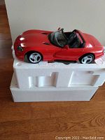 Red Chrysler Viper 1:12 scale die-cast model placed on white foam packaging, showing car profile and details.