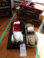 Photo of three die cast model cars, including the red 1963 Thunderbird Roadster in box, and white and gold models on display base