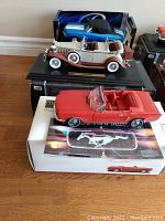 Overview of three model cars displayed on stands and boxes: blue Chevelle at center, beige Cadillac behind, red Mustang at front.